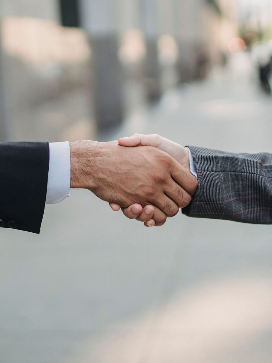 Two people in business dress shaking hands on a city street